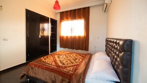 A bedroom with a bed, a wardrobe, a window with curtains, and a hanging red light fixture. - amazing appartement in center city (Marrakesh)