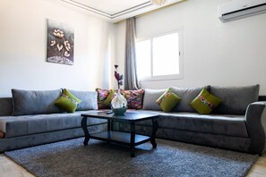 A living room with a grey sofa, colorful cushions, a glass coffee table, and a painting on the wall. - amazing appartement in center city (Marrakesh)