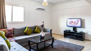 A modern living room with a grey sofa, colorful cushions, a black coffee table, a TV, and a chandelier. - amazing appartement in center city (Marrakesh)