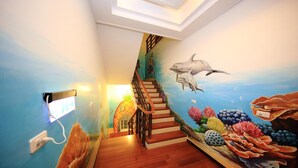 Een trap met een muurschildering van zeedieren, leidend naar een kamer met uitzicht op de oceaan.