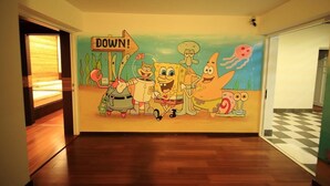Een gang met een muurschildering van tekenfiguren en een bord met de tekst 'DOWN'.