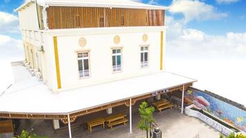 Um edifício branco com telhado plano, um alpendre coberto com bancos de madeira e um mural com vida marinha na parede.
