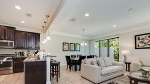 A modern kitchen with dark cabinets, a central island, and a dining area with a white sofa and chairs. - Elegant and Spacious 4BD Home Near Disney and Minutes From Florida's top Golf Courses! #8197 (Davenport)