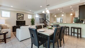 A spacious living area with a dining table set for four, a white sofa, and a TV. - Elegant and Spacious 4BD Home Near Disney and Minutes From Florida's top Golf Courses! #8197 (Davenport)