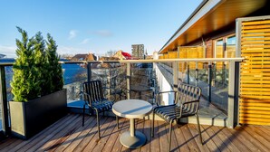 Eine Holzterrasse mit einem runden Tisch und zwei Stühlen, mit Blick auf eine Stadtlandschaft.