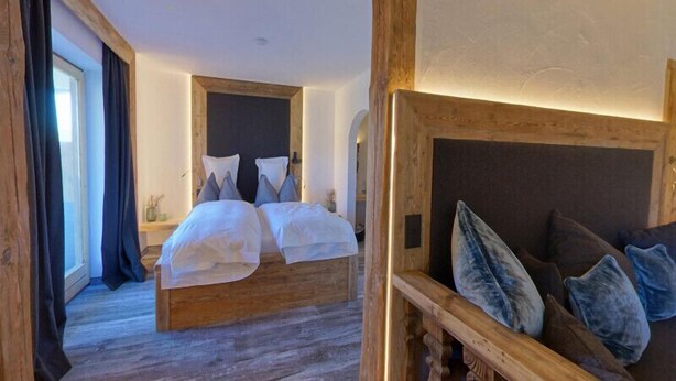 A bedroom with a large bed, wooden headboard, and a view of the outdoors. - Hotel Gasthof Eder (Gmund am Tegernsee)