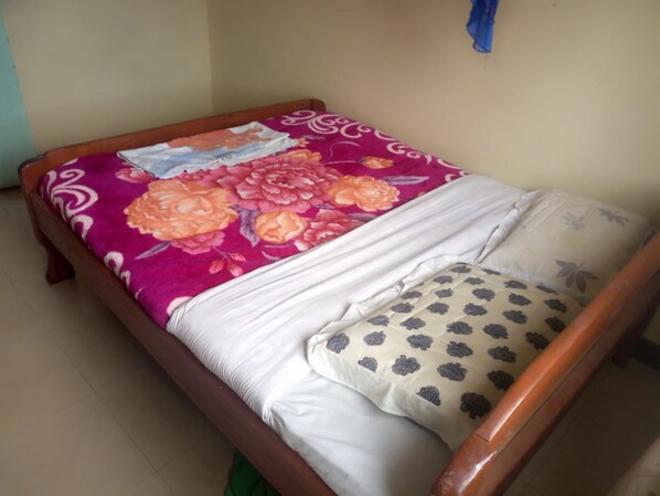 A bed with a floral bedspread, white pillows, and a wooden frame. - Goodmorning Hotel (Kisii)