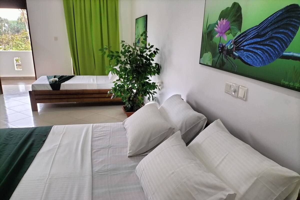 A bedroom with a bed, pillows, a green plant, and a painting of a butterfly.