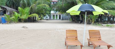 Une plage avec deux chaises longues en bois et un parasol vert et noir.