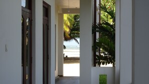 Un pasillo que da a vista de playa, con una palmera y un pequeño panel verde en la pared.