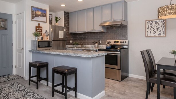 A modern kitchen with grey cabinets, a central island with stools, stainless steel appliances, and a decorative wall piece. - Modern Condo with Shared Hot Tub! Short Walk to Village! (Mammoth Lakes)