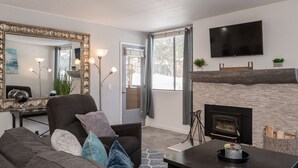 A modern living room with a fireplace, a large mirror, a flat-screen TV, and a cozy seating area. - Modern Condo with Shared Hot Tub! Short Walk to Village! (Mammoth Lakes)