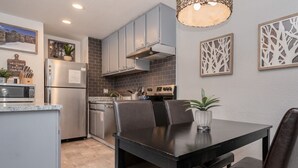 A modern kitchen with grey cabinets, a stainless steel refrigerator, a built-in oven, and a dining area with a black table and chairs. - Modern Condo with Shared Hot Tub! Short Walk to Village! (Mammoth Lakes)