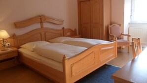 Een slaapkamer met een houten bed, nachtkastje, stoel en een kledingkast.