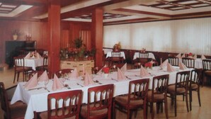 Een feestzaal met meerdere gedekte tafels, houten stoelen en een decoratief plafond.