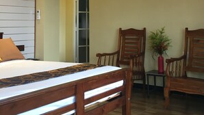 A hotel room with a bed, two wooden chairs, a small table with a vase, and a painting on the wall. - Villa Forest View (Kandy)