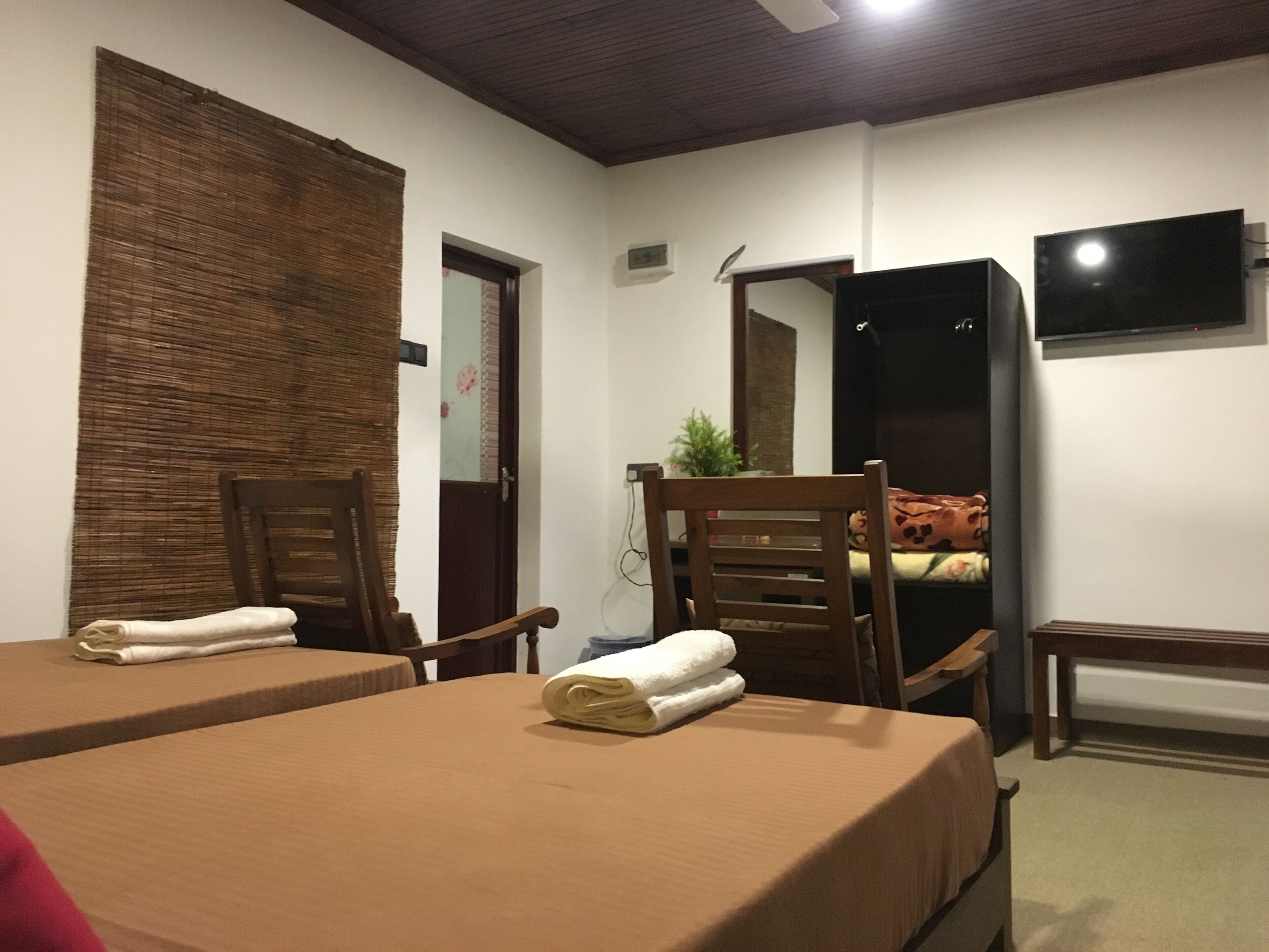 A hotel room with two beds, a wooden chair, a small table, a TV, and a mirror.