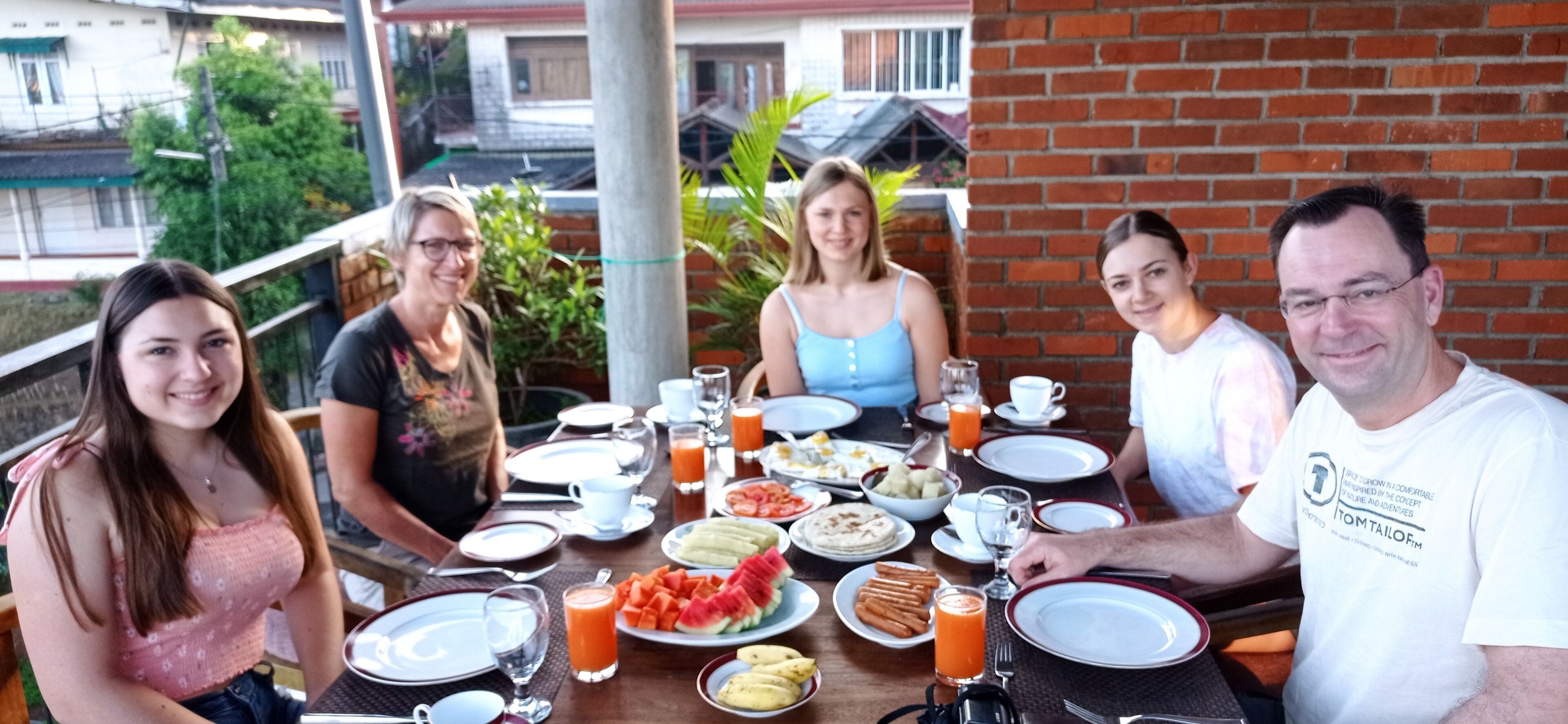 A group of people seated at an outdoor table with various breakfast items, including fruits, pastries, and beverages.