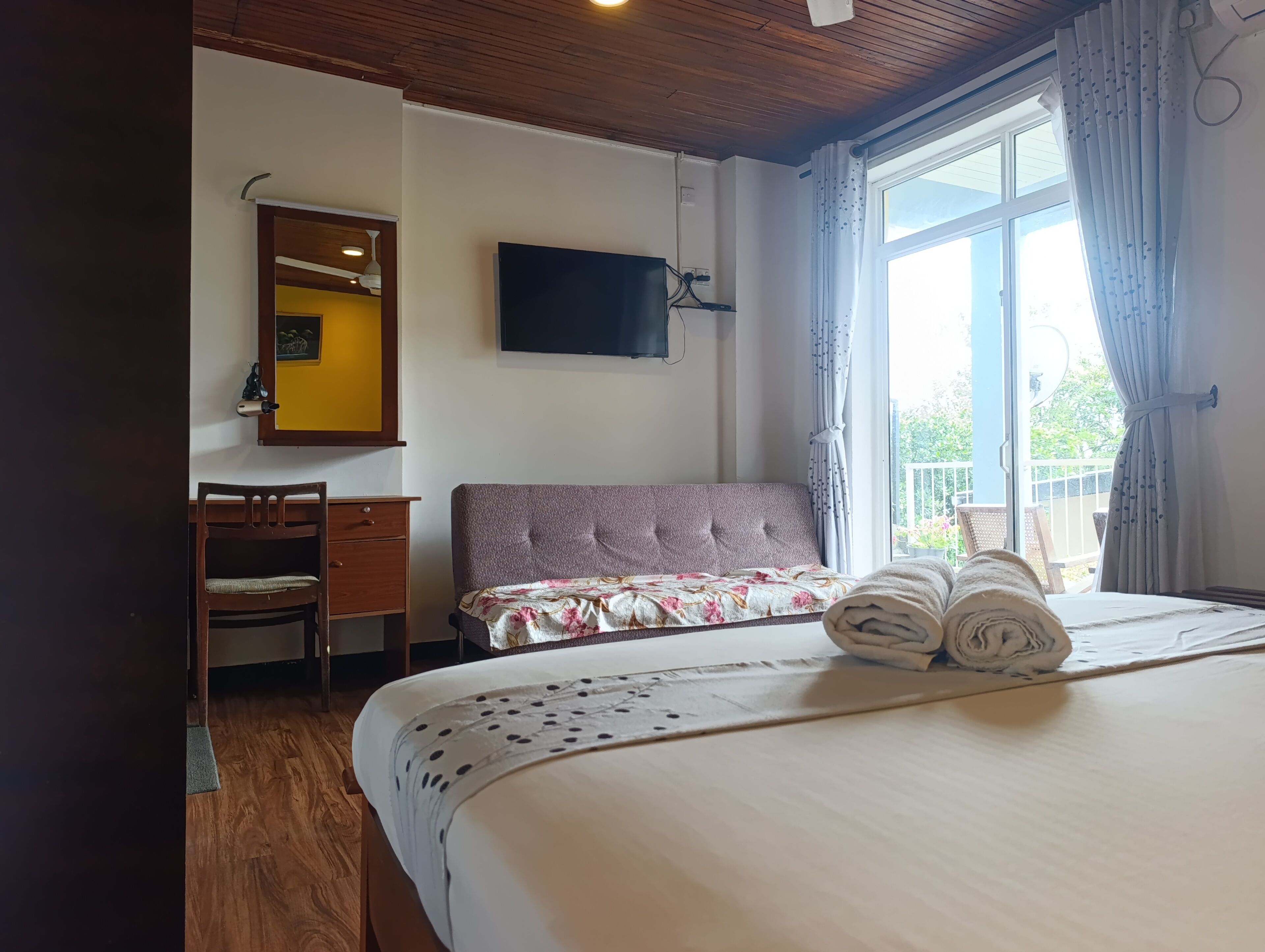 Un dormitorio con una cama, un escritorio, una silla, un televisor y una ventana con cortinas.