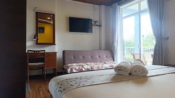 Un dormitorio con una cama, un escritorio, una silla, un televisor y una ventana con cortinas.