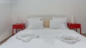 A neatly made bed with white linens, two red nightstands, and a beige pillow. - Apartment Piano (Belgrade)