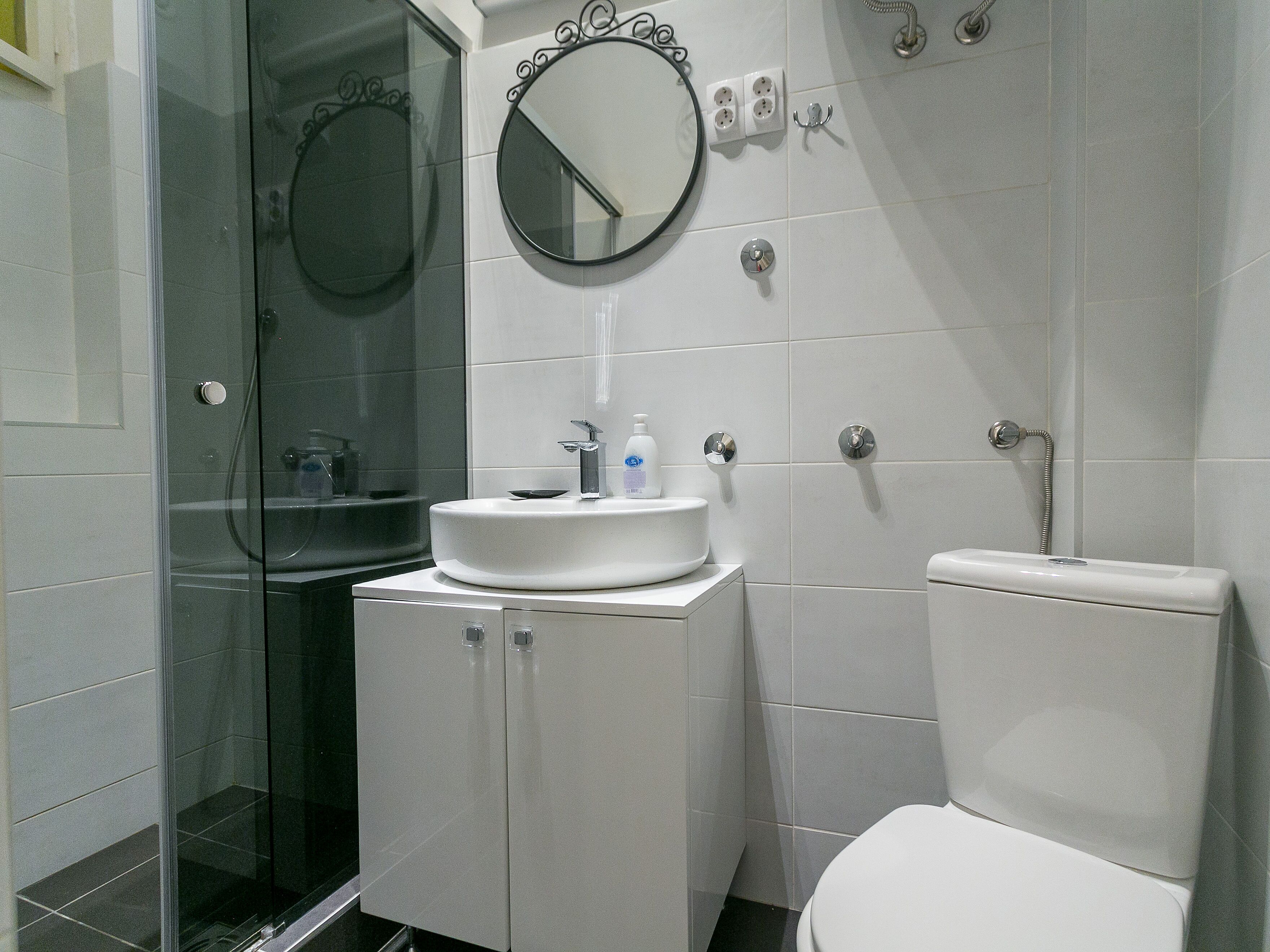 Een badkamer met een glazen douchecabine, een wastafel met spiegel erboven en een toilet.