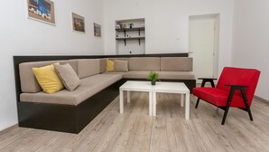 A modern living room with a sectional sofa, a red chair, a white coffee table, and shelves with books and plants. - Apartment Piano (Belgrade)