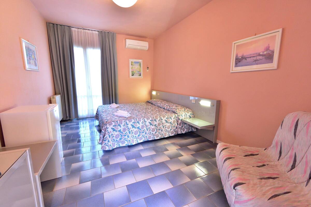 Un dormitorio con cama, una silla, un escritorio y una ventana con cortinas.
