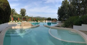 Piscina con sillas de descanso y sombrillas, rodeada de árboles y vistas a colinas.