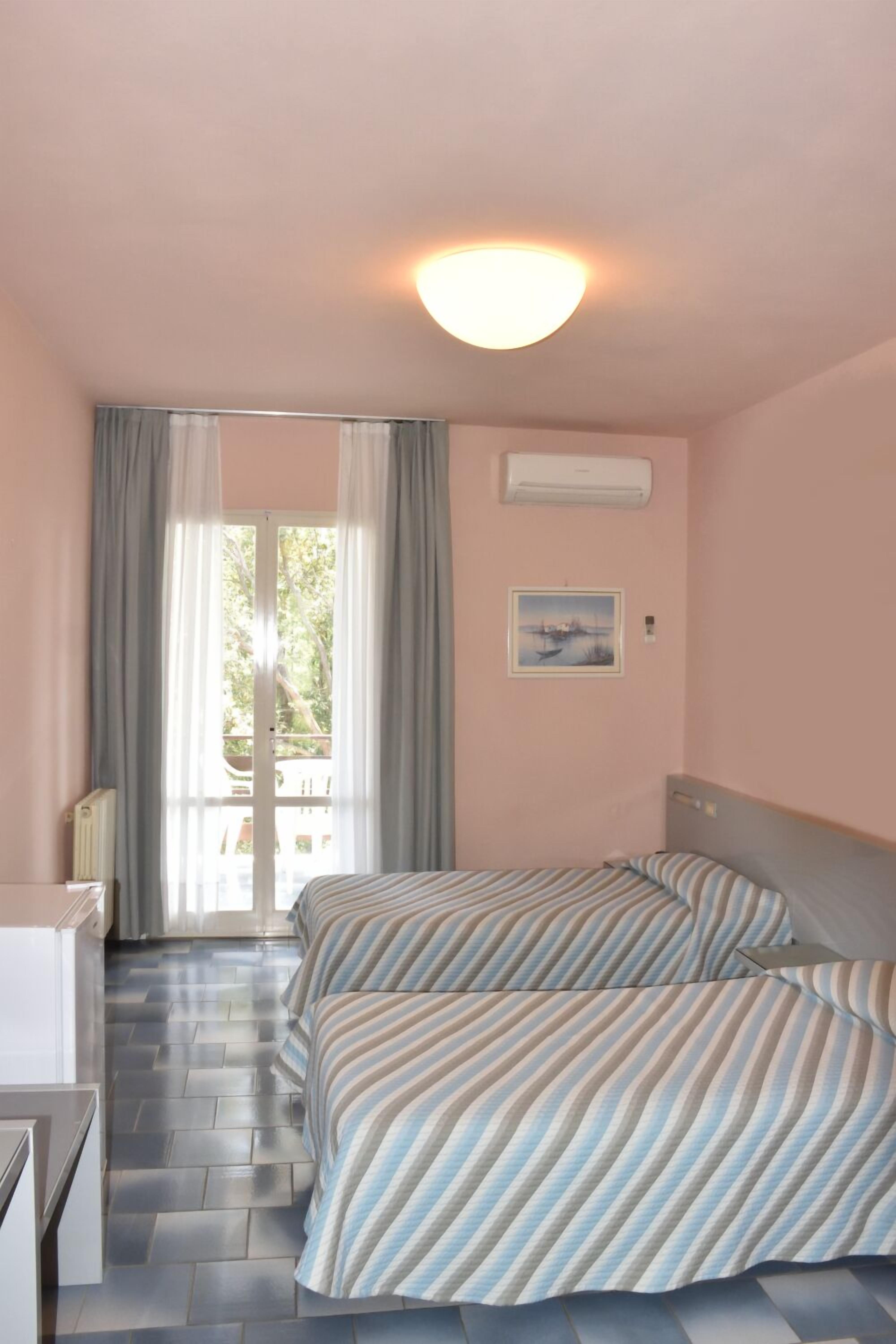 Hotellihuone, jossa on sänky, työpöytä, tuoli, ikkuna verhoilla ja taulu seinällä.
