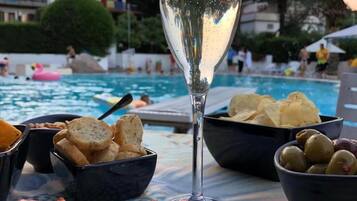 Ein Tisch mit Speisen und einem Glas Wasser am Poolrand.