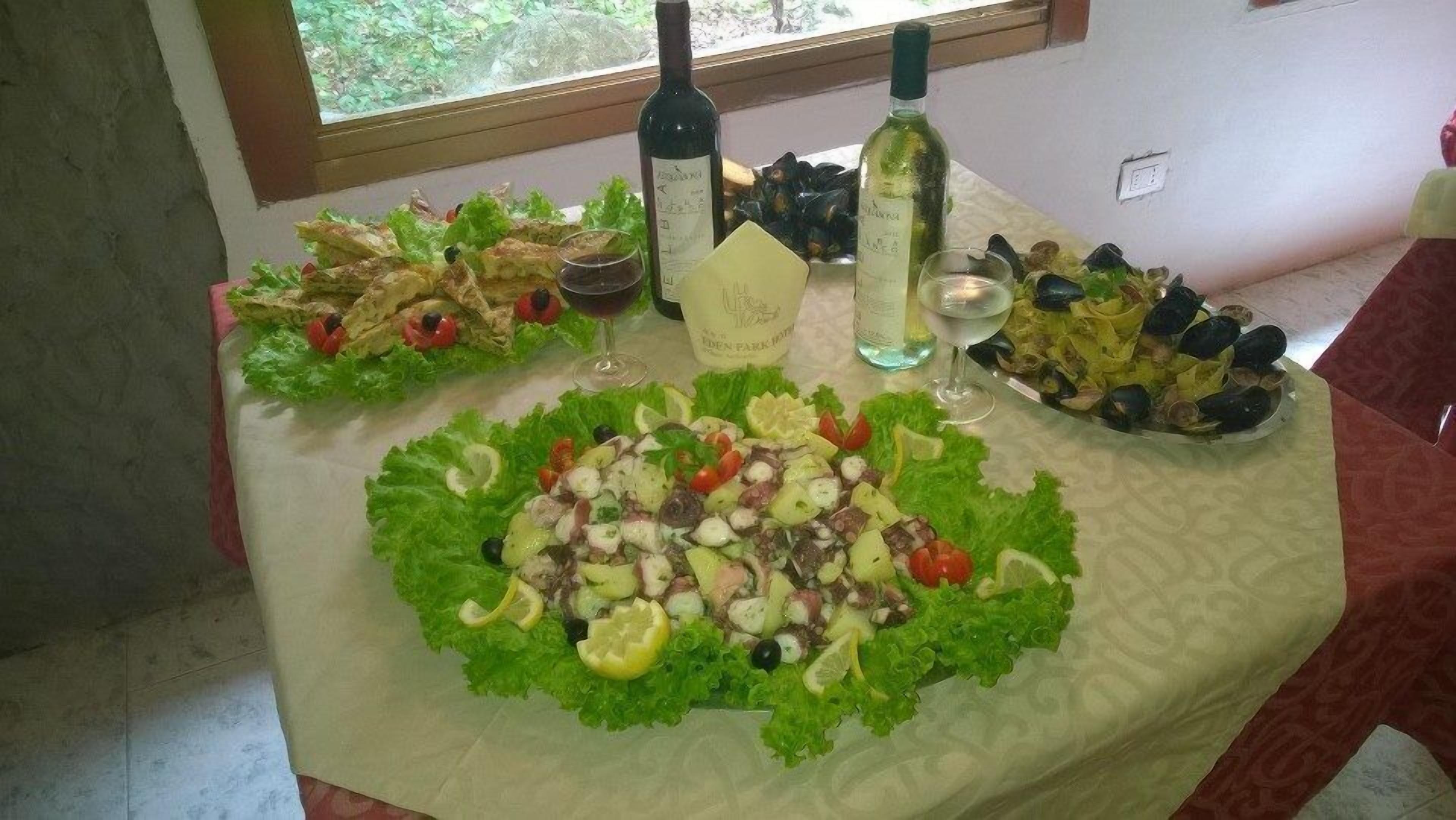 A table with various salads and two bottles of wine.