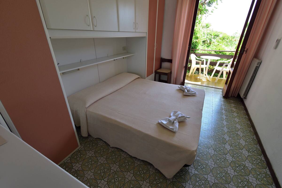 Habitación pequeña con cama individual, balcón y vista a zonas verdes.