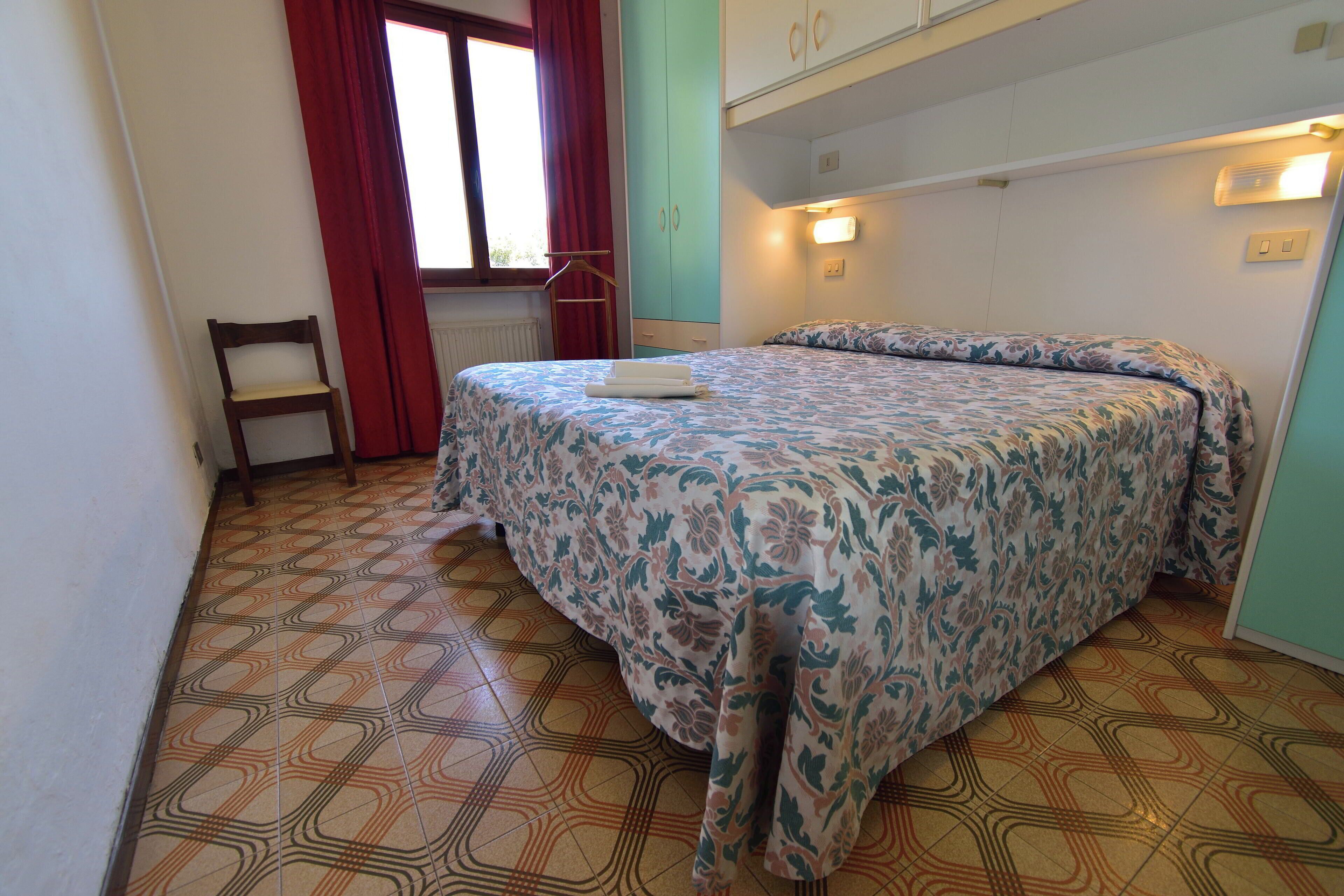 Une chambre à coucher avec un lit, une chaise, une armoire et une fenêtre avec des rideaux.