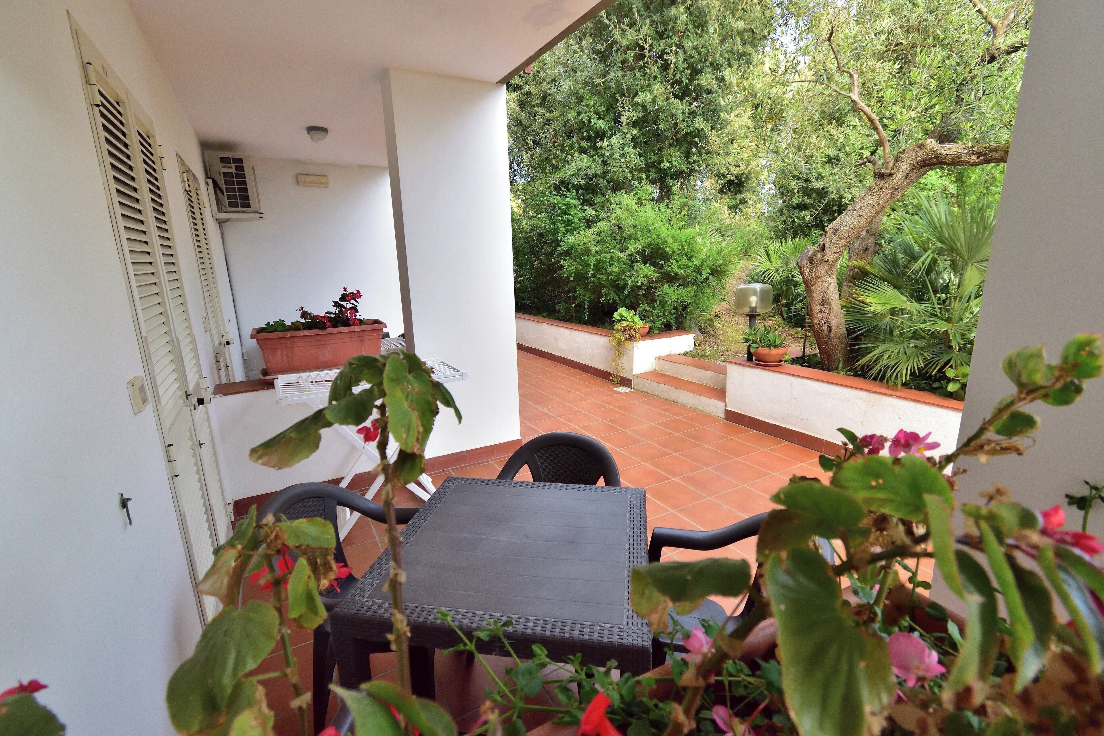 A patio with a table and chairs, surrounded by potted plants and a view of a garden.