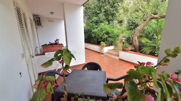 A patio with a table and chairs, surrounded by potted plants and a view of a garden.