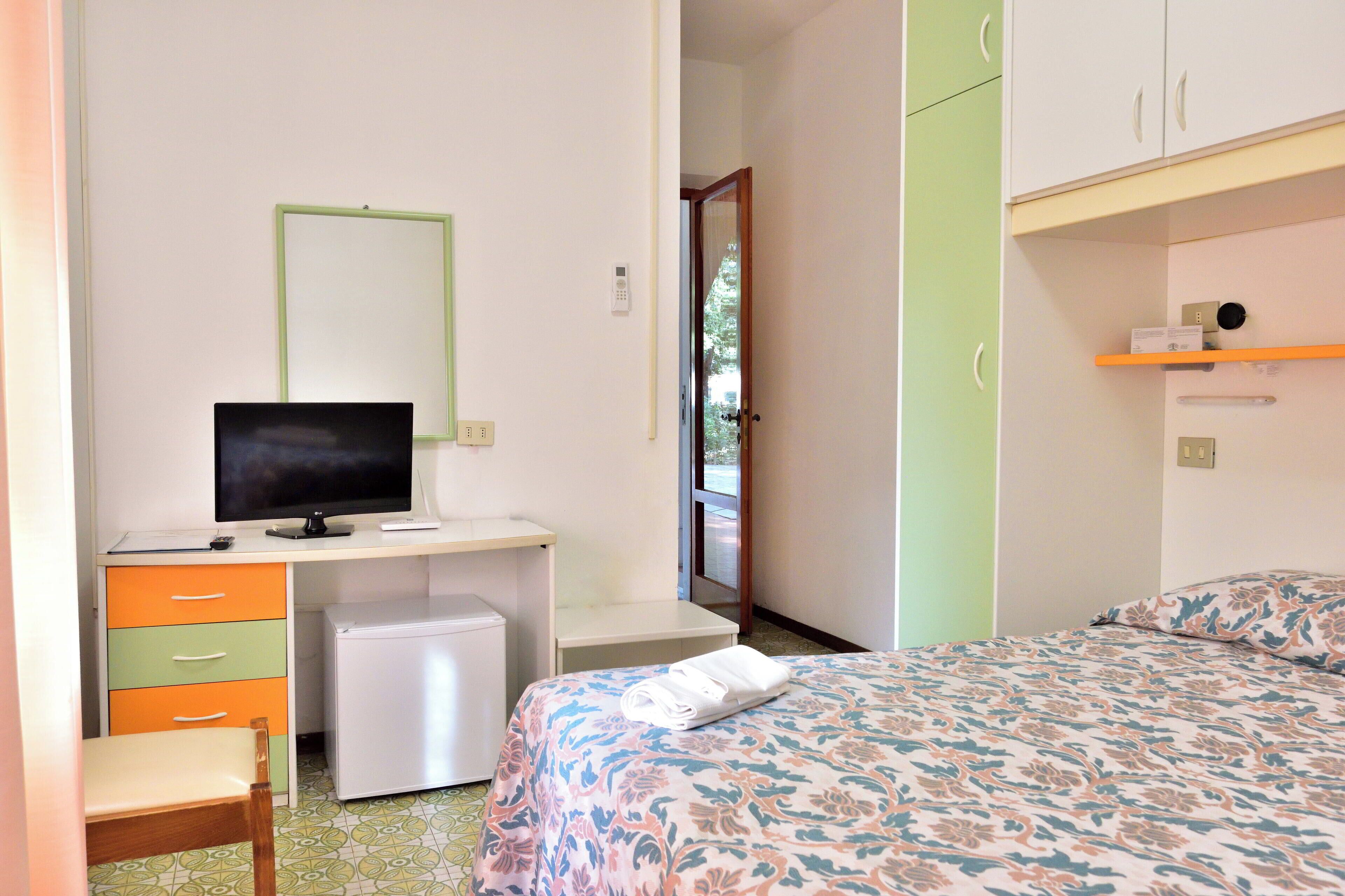 Une chambre comprenant un lit, un bureau avec un ordinateur, un petit réfrigérateur et une chaise.