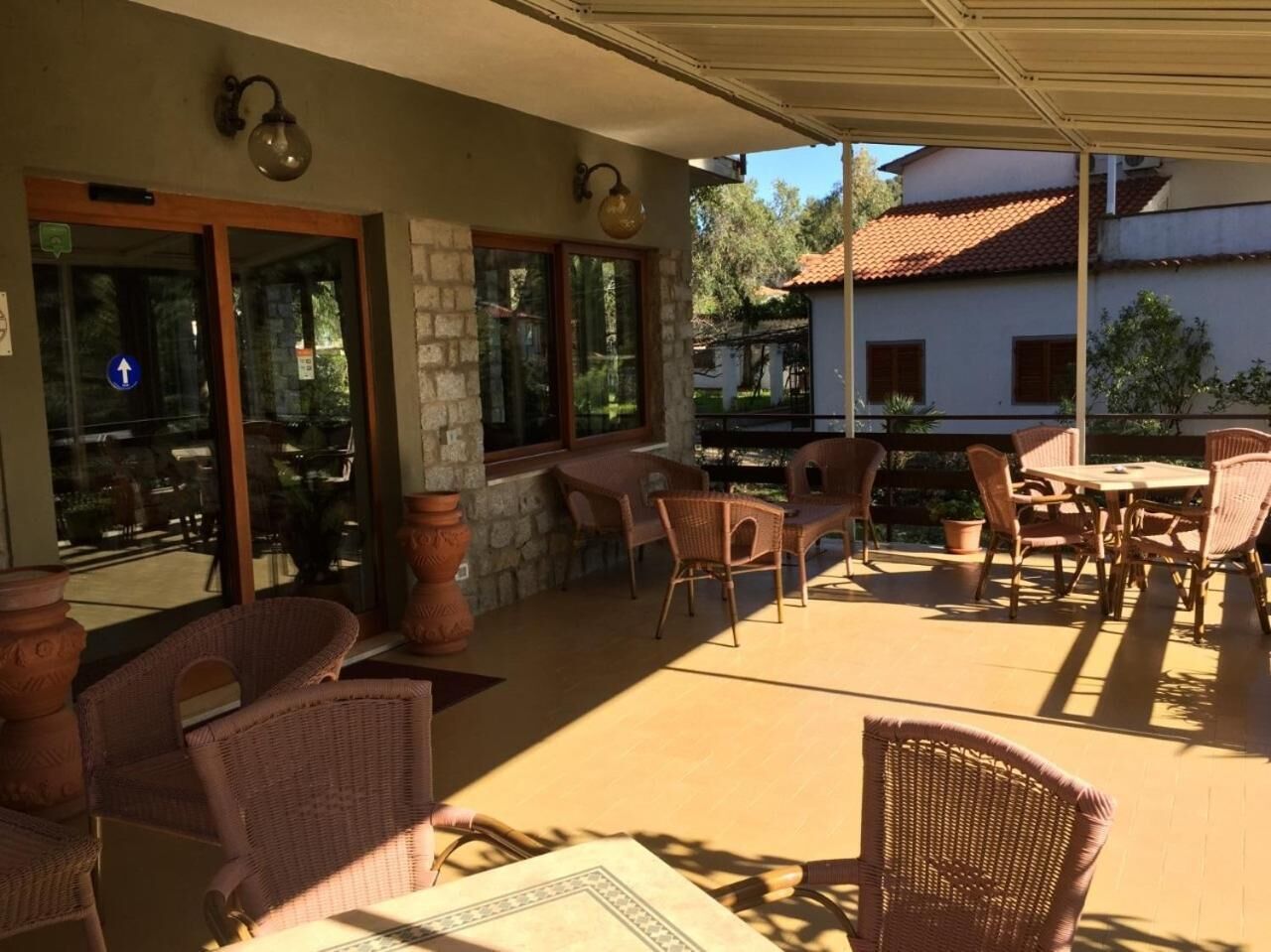 Un espace extérieur aménagé en terrasse, avec des meubles en osier, des piliers en pierre et une vue sur les bâtiments environnants.