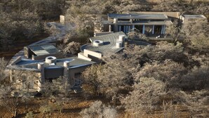 Une maison moderne dotée d’un toit incurvé, entourée d’arbres et située dans un paysage aride.