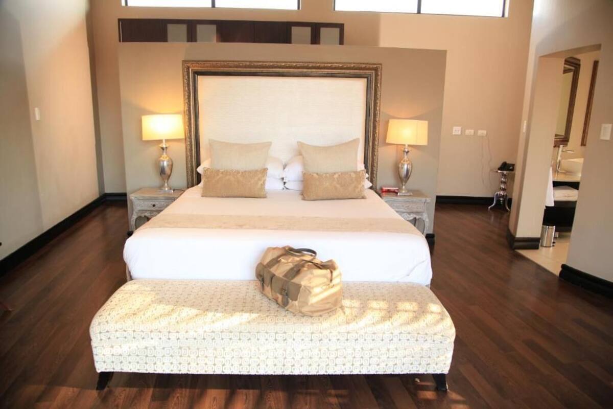 A large bed with a headboard, two bedside tables with lamps, a bench at the foot of the bed, and a bag on the bench.