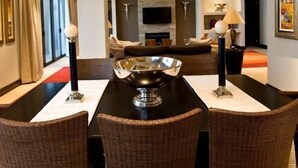 Un espace repas moderne avec une table noire, trois chaises en osier et un grand vase décoratif placé au centre.