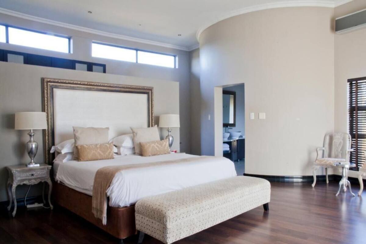 A spacious bedroom with a large bed, two bedside tables with lamps, a bench, and a chair.