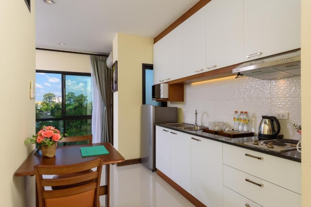 Una cocina compacta con armarios blancos, un refrigerador de acero inoxidable y una ventana con vistas a la vegetación.