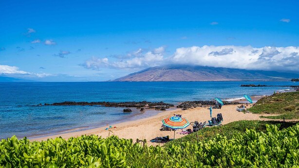 A beach with clear skies, a mountain in the background, and a few umbrellas. - Kamaole Sands 3-308, Premier Location, Renovated, Large Lanai, Wi-Fi, Split AC!  (Kihei)