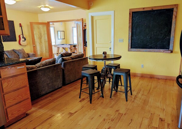 Un salon chaleureux avec un plancher en bois, un canapé, une table basse et un coin repas équipé de tabourets.