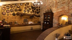 Une cuisine rustique aux murs en briques apparentes, agrémentée de différents ustensiles de cuisine suspendus et d’un meuble en bois contenant des bouteilles.
