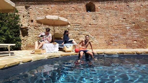 Un espace piscine avec un mur en pierre en arrière-plan, un banc et un parasol pour faire de l’ombre.