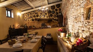 Un coin repas accueillant, avec une table dressée pour deux personnes, entouré de murs en pierre et agrémenté de divers ustensiles de cuisine.
