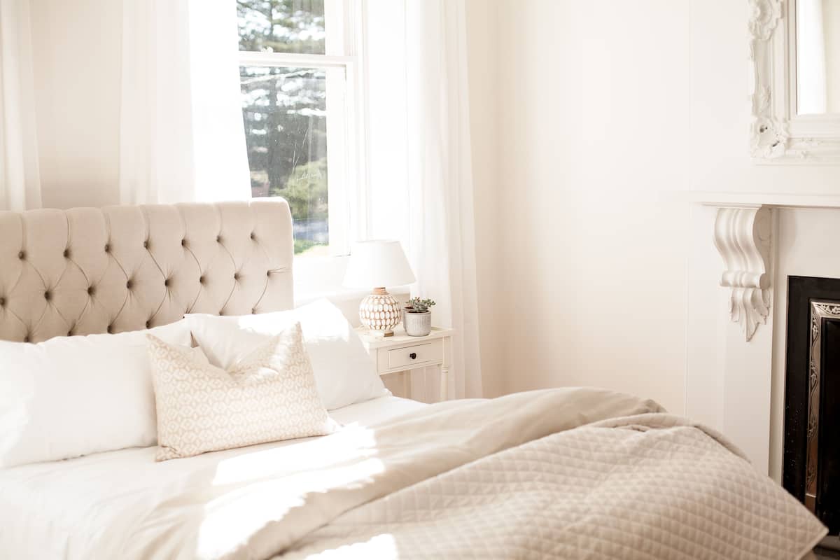 A neatly made bed with a tufted headboard, a bedside table with a lamp, and a fireplace.
