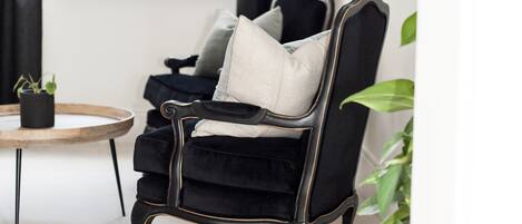 Un sillón negro con un cojín blanco, una mesita redonda con una planta y un ventanal con cortinas.